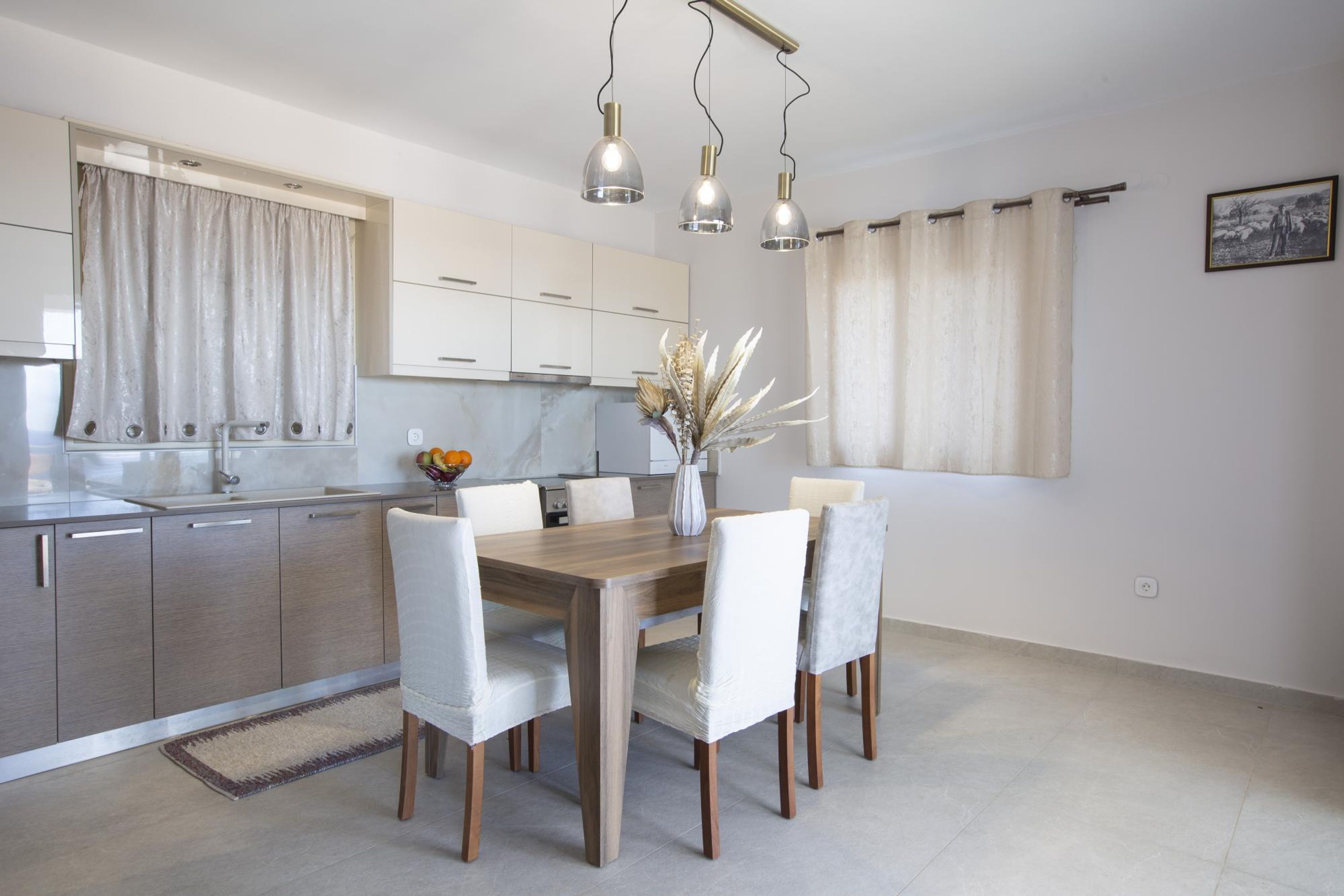 A modern kitchen with a wooden dining table, white chairs, and pendant lighting.