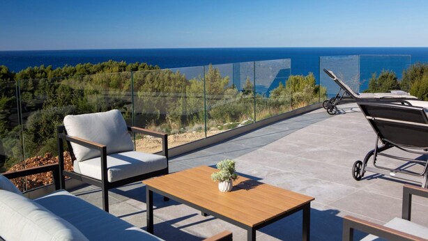 Terraço no telhado com vista clara do mar, mobiliado com sofá, mesa e poltrona.
