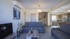 Uma sala de estar moderna com televisão de tela plana, sofás cinzas, uma mesa de centro e uma escada que leva a uma cozinha.