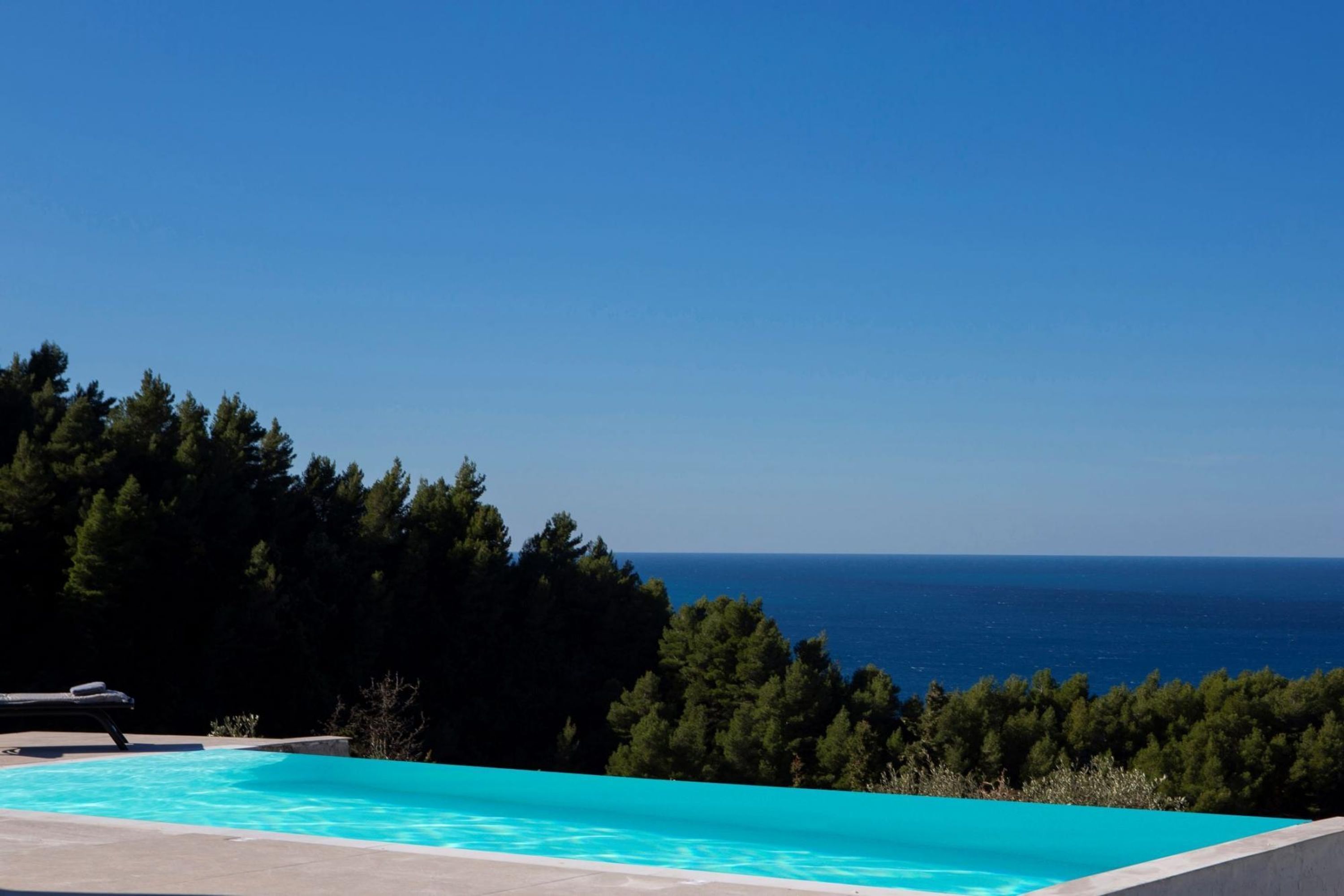 Une piscine offrant une vue dégagée sur l’océan et une colline boisée.