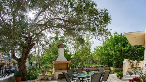 An outdoor patio with a stone floor, a round table with chairs, a chimney, and potted plants. - Nikis Country House - Lefkada BnB  Private Parking (Ligia)