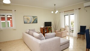 A living room with a sofa, a TV, a bookshelf, and a chair. - Nikis Country House - Lefkada BnB  Private Parking (Ligia)