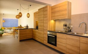 A modern kitchen with wooden cabinets, a built-in oven, and a stainless steel sink. - Heartwood Suite w Shared Pool by Roots Suites (Agios Nikolaos)