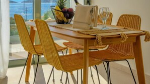 A dining area with a view of the sea, featuring wicker chairs, a wooden table, and hanging wicker lamps. - Branch Suite w Shared Pool by Roots Suites (Agios Nikolaos)