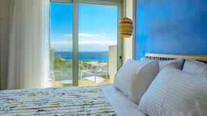 A bedroom with a large bed, a view of the sea, and a balcony with a table and chairs. - Branch Suite w Shared Pool by Roots Suites (Agios Nikolaos)
