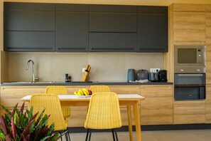 Eine moderne Küche mit dunklen Schränken, einer Edelstahlspüle, einem eingebauten Backofen und einem Essbereich mit gelben Stühlen.