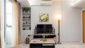 A modern living room with a flat-screen TV, a coffee table with decorative items, a bookshelf, and a lamp. - Sky 7 View Apartment (Heraklion)