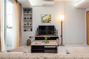 A modern living room with a flat-screen TV, a coffee table with decorative items, a bookshelf, and a lamp. - Sky 7 View Apartment (Heraklion)