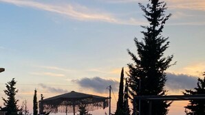 Ein Swimmingpool mit Liegestühlen und einer Pergola, umgeben von Bäumen und Blick auf den Sonnenuntergang.