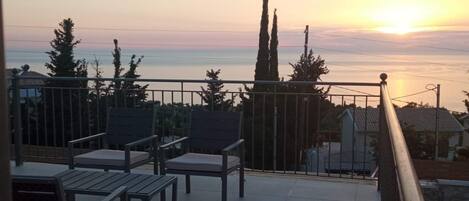 Una terraza con sillas y barandilla que da a un cuerpo de agua al atardecer.