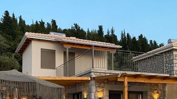 Ein zweistöckiges Haus mit Natursteinfassade, einem Balkon und einer überdachten Sitzterrasse mit Liegestühlen.