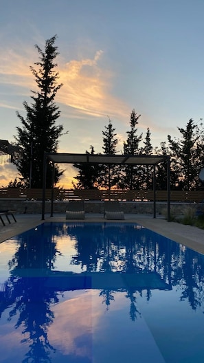 A swimming pool with a clear view of the sunset and surrounding trees.