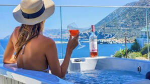 Eine Person entspannt in einer Hot Tub mit einer Weinflasche und einem Glas, mit Blick auf eine malerische Wasserlandschaft und Berge.