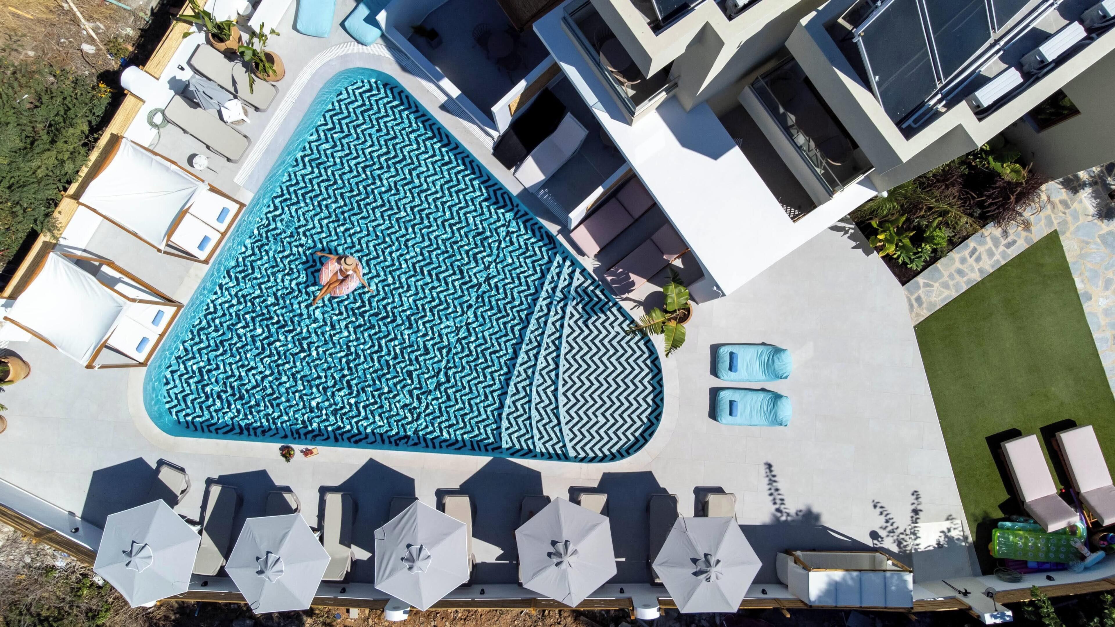 An aerial view of a swimming pool with geometric patterns, surrounded by lounge chairs and umbrellas.