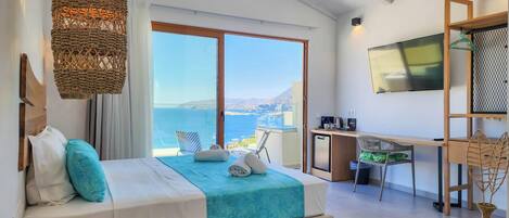A bedroom with a bed, a desk, a TV, and a view of the sea.