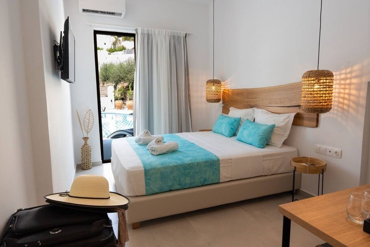 Une chambre d’hôtel avec un lit, un téléviseur fixé au mur, une petite table et une valise.