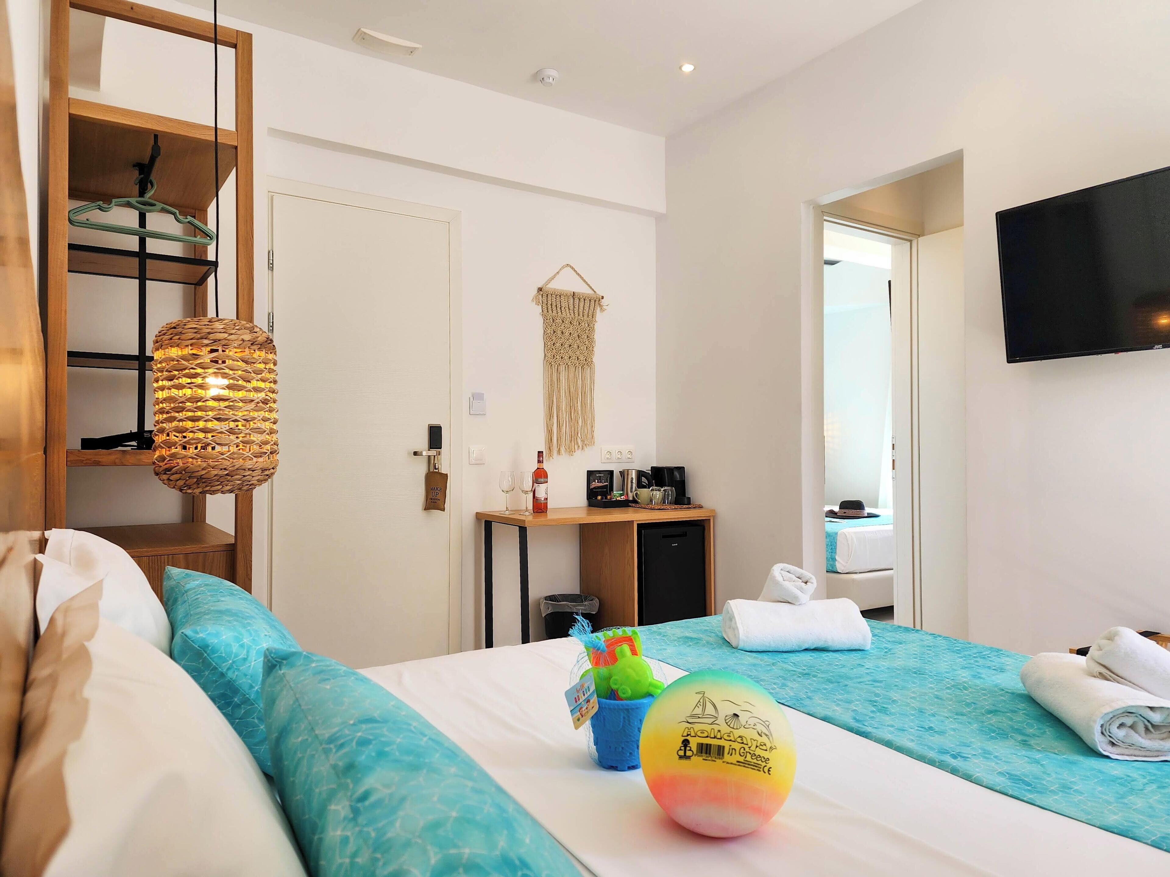 A hotel room with a bed, a desk with a coffee maker, a TV, and a door leading to a bathroom.