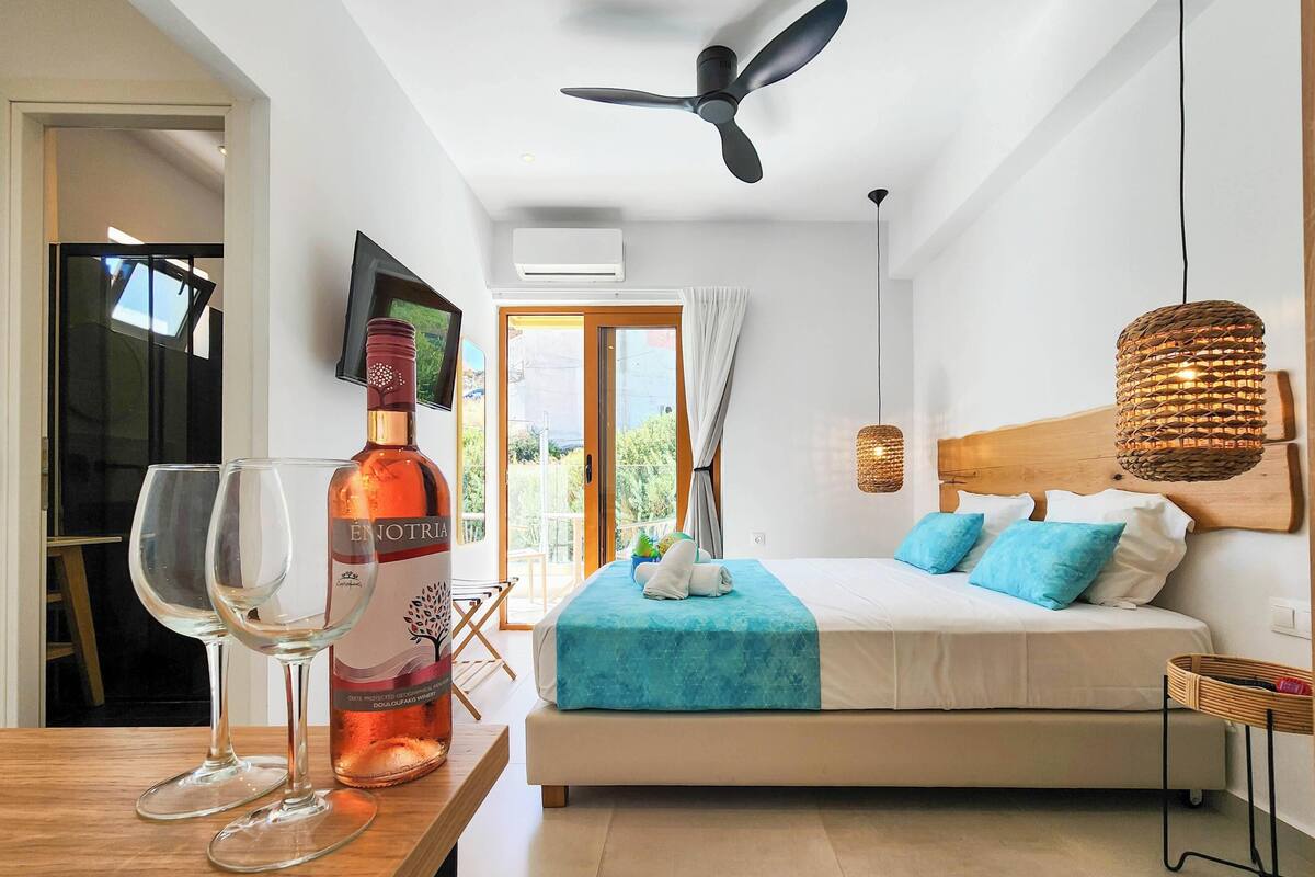 Une chambre d’hôtel avec un lit, un ventilateur de plafond, une télévision, une bouteille de vin et une vue sur l’extérieur.
