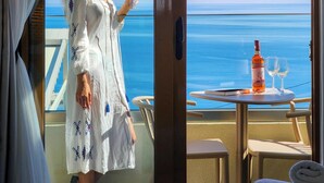 Ein Zimmer mit Balkon und Meerblick, ein Tisch mit Flasche und Gläsern sowie ein Bett mit zusammengelegtem Handtuch.