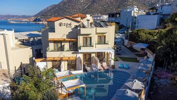 A hotel with a pool, outdoor seating, and a view of the sea.