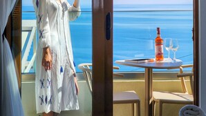 Ein Zimmer mit Meerblick, ein Tisch mit einer Flasche und Gläsern, und eine Person, die ein Glas hält.