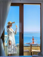 Una habitación con vista al mar, una mesa con una botella y vasos, y una persona sosteniendo un vaso.