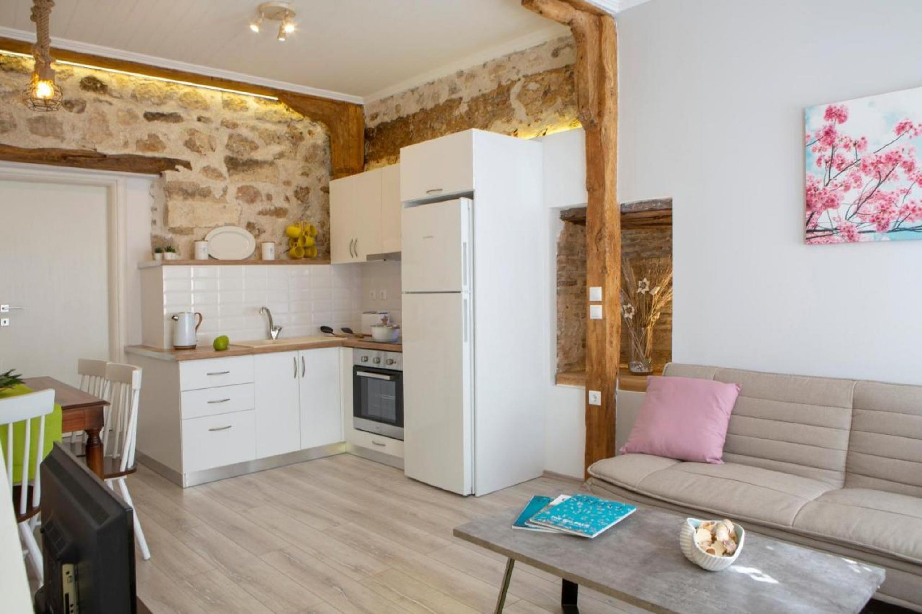 Une cuisine moderne avec des meubles blancs, un four encastré et un réfrigérateur. On y trouve une table à manger avec des chaises, un canapé et une table basse.