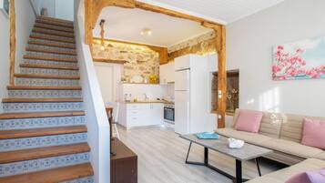 Une cuisine moderne avec des meubles blancs, un escalier en bois et un canapé beige agrémenté de coussins roses.