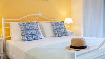 Un lit bien fait, agrémenté d’oreillers à motifs, d’une tête de lit blanche et d’un chapeau posé sur le lit.