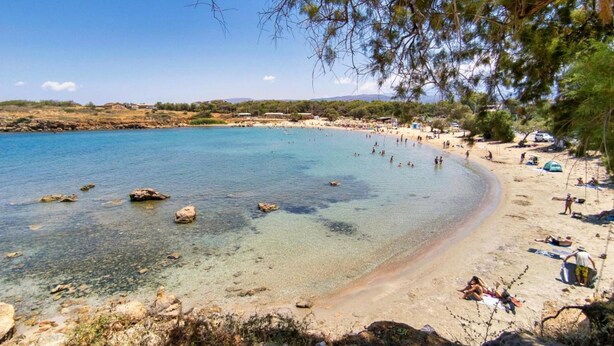 Ein Strand mit klarem Wasser, Felsen und Personen.