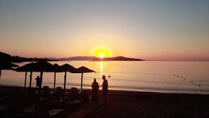 Ein Strand mit Sonnenschirmen und Liegestühlen, ein Sonnenuntergang und ein ruhiges Meer.