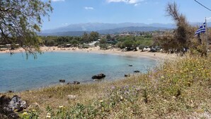 Eine Küstenlandschaft mit Strand, klarem blauen Wasser und Bergen im Hintergrund.
