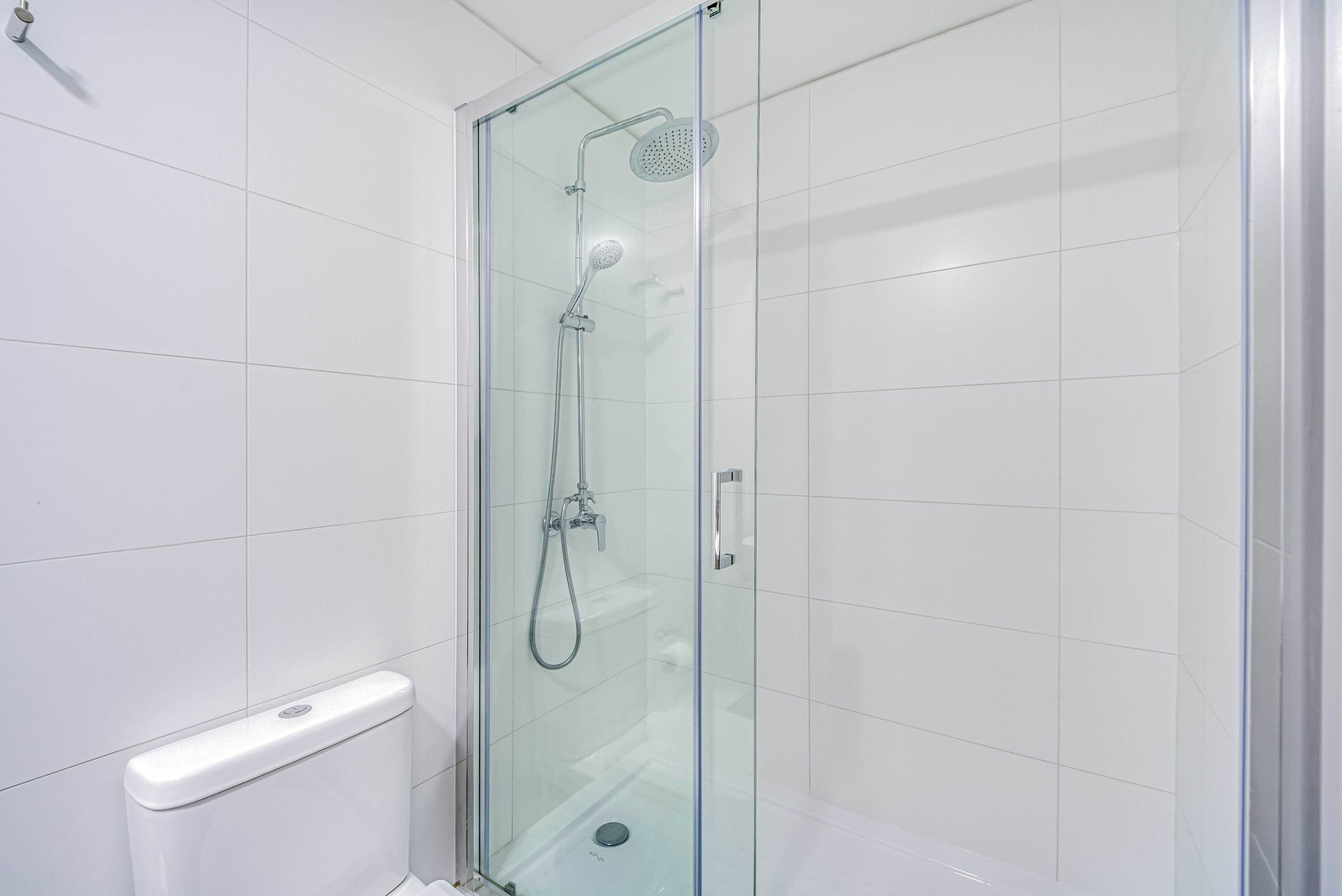 Une douche fermée par des parois en verre, dotée d’un pommeau de douche à main et d’un robinet mural.