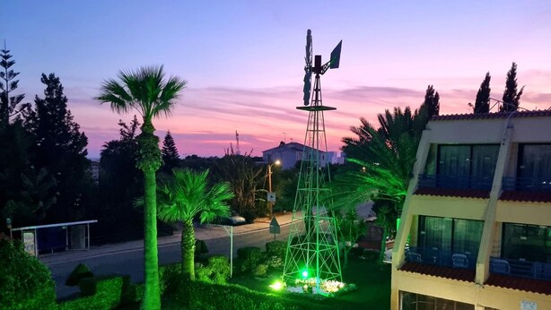 A modern building with a flat roof and large windows, surrounded by well-maintained greenery and a clear sky. - Apartment with Pool View (Ayia Napa)