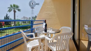 A balcony with a table and chairs, a bottle of wine, and a windmill in the background. - Apartment with Pool View (Ayia Napa)