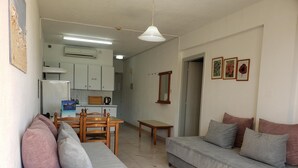 Een woonkamer met een bank, een eettafel en een keuken met kasten en een airconditioner.