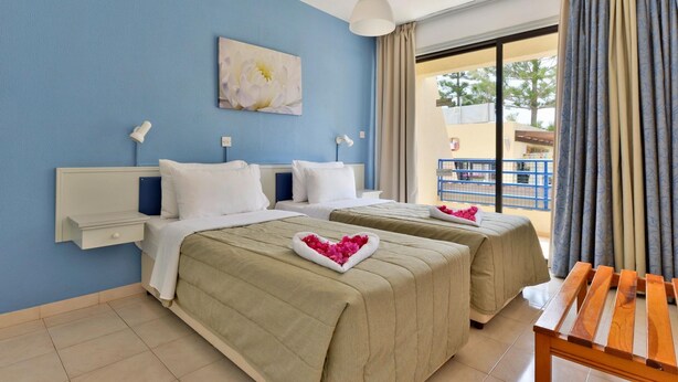 Een hotelkamer met twee bedden, een tafeltje, een nachtkastje en een raam met gordijnen.