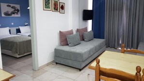 Een hotelkamer met een grijze bank, een houten eettafel, een aan de muur bevestigde televisie en een bed met wit beddengoed.