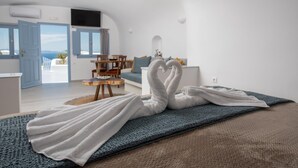 Quarto com cama, um tapete azul e duas toalhas dobradas em formato de cisne. Uma mesa de madeira e uma cadeira ao fundo.