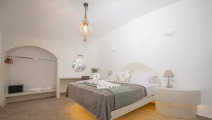 A modern bedroom with a bed, bedside table, and a hanging light fixture. - Luxury Cave Suite | Jetted Tub | Sea & Sunset View (Oía)