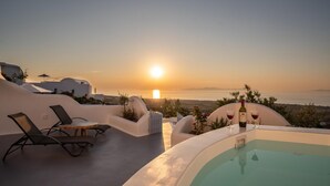 A sunset view from a rooftop terrace with a pool, lounge chairs, and a bottle of wine. - Luxury Cave Suite | Jetted Tub | Sea & Sunset View (Oía)