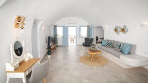 Uma sala de estar ampla com teto branco e curvo, um conjunto de sofás, uma escrivaninha de madeira e uma cadeira.