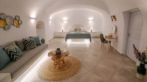 Quarto moderno com teto curvo, cama com colcha verde, pequena escrivaninha com cadeira, sofá com almofadas estampadas e arte decorativa na parede.