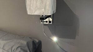 Une salle de bain avec une pomme de douche fixée au mur, une serviette suspendue à un porte-serviettes et un lit recouvert d’une couverture à motifs.