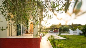 Un bâtiment à la façade rouge et blanche, un chemin menant à une zone abritée et de la verdure au premier plan.