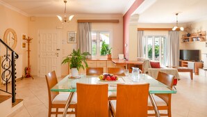 Un vaste espace de vie comprenant une table à manger en verre, des chaises en bois, un canapé et un téléviseur.