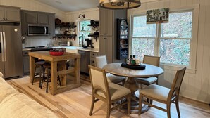 A modern kitchen with wooden cabinetry, a central island, and a dining area with four chairs. - Cozy cottage on the river and minutes from Dahlonega. (Dahlonega)
