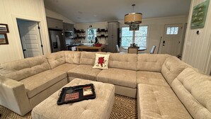 A large L-shaped sectional sofa with a tray table in front, a patterned rug, and a dining area in the background. - Cozy cottage on the river and minutes from Dahlonega. (Dahlonega)