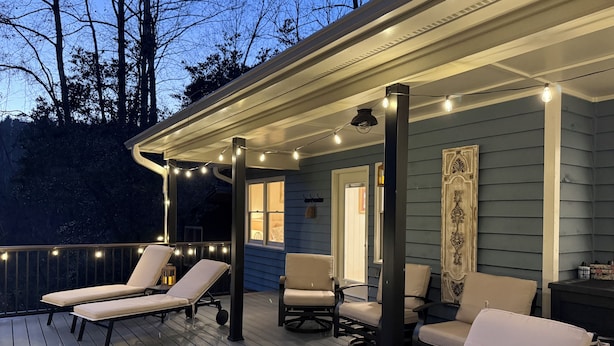 A covered deck with lounge chairs and string lights. - Cozy cottage on the river and minutes from Dahlonega. (Dahlonega)