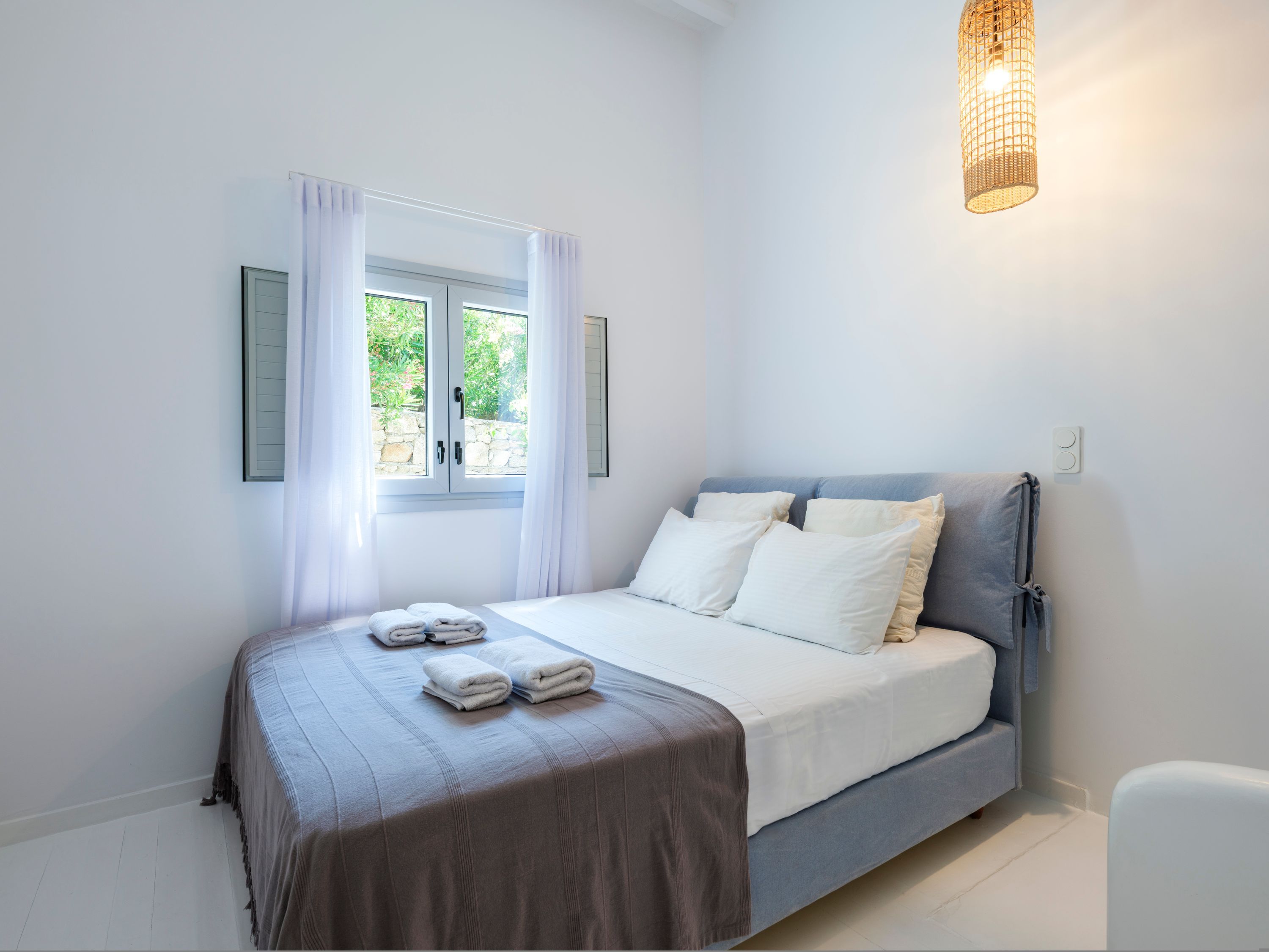 A bedroom with a bed, a window with curtains, a bedside lamp, and a wall-mounted light switch.
